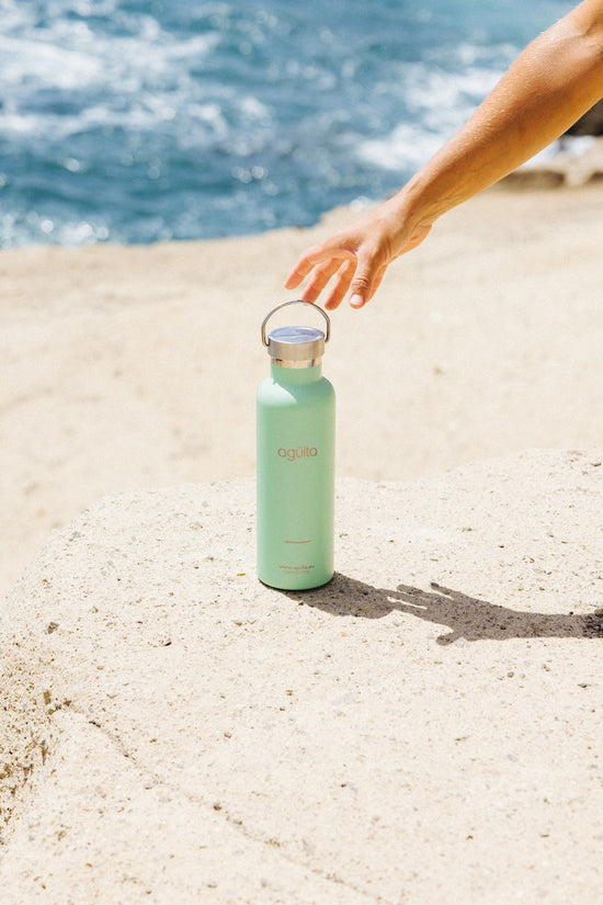 A hand picking up a sea green insulated Agüita water bottle