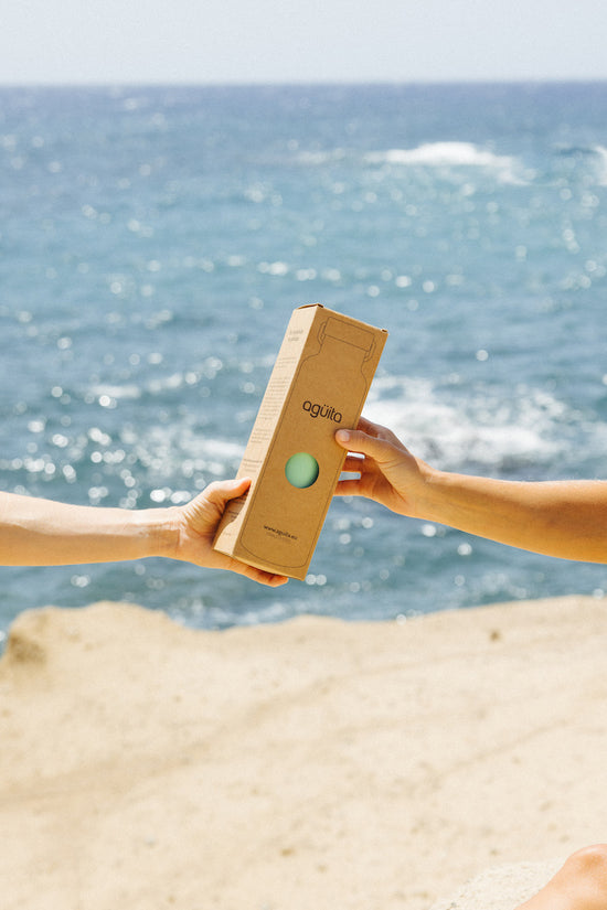 A hand giving to another hand a box containing an Agüita bottle